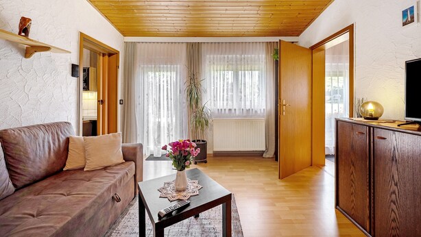 Ein Wohnzimmer mit Holzboden, einer Couch, einem Couchtisch mit einer Vase und einem Fernseher auf einer Holzkommode.