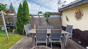 Eine Terrasse im Freien mit einem Holztisch, Stühlen, einer Satellitenschüssel und einer Dekowand.