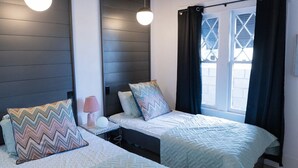 Ein Hotelzimmer mit zwei Betten, einem Nachttisch, einer Lampe und einem Fenster mit Vorhängen.