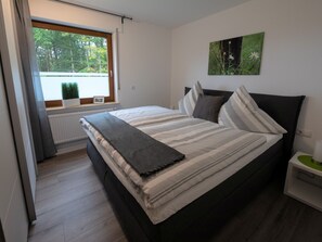 Ein Schlafzimmer mit Bett, Fenster, Heizkörper, Nachttisch und einem Bild an der Wand.