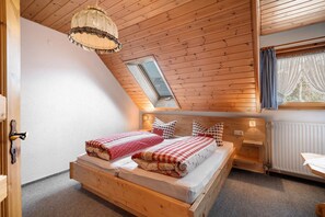 Une pièce avec un plafond en pente, un lit avec une couette à carreaux, une fenêtre avec des rideaux et une tête de lit en bois.