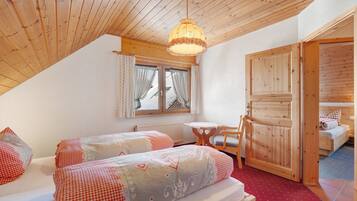A cozy room with two beds, a wooden ceiling, a window with curtains, and a small table.