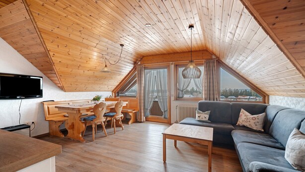 Ein gemütlicher Loftraum mit Holzbalkendecke, einem Essbereich, einer Couch und einem an der Wand befestigten Fernseher.