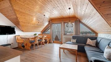 Une pièce confortable de style loft, avec un plafond en bois, un coin repas, un canapé et un téléviseur fixé au mur.