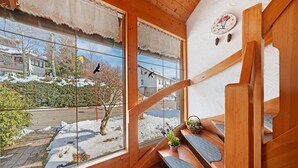 Eine Holztreppe mit Blick auf eine verschneite Landschaft und ein Haus im Hintergrund.