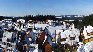 Ein schneebedecktes Dorf mit traditionellen Häusern, wolkenlosem Himmel und Bergen in der Ferne.