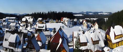 A snow-covered village with traditional houses, a clear sky, and distant mountains.