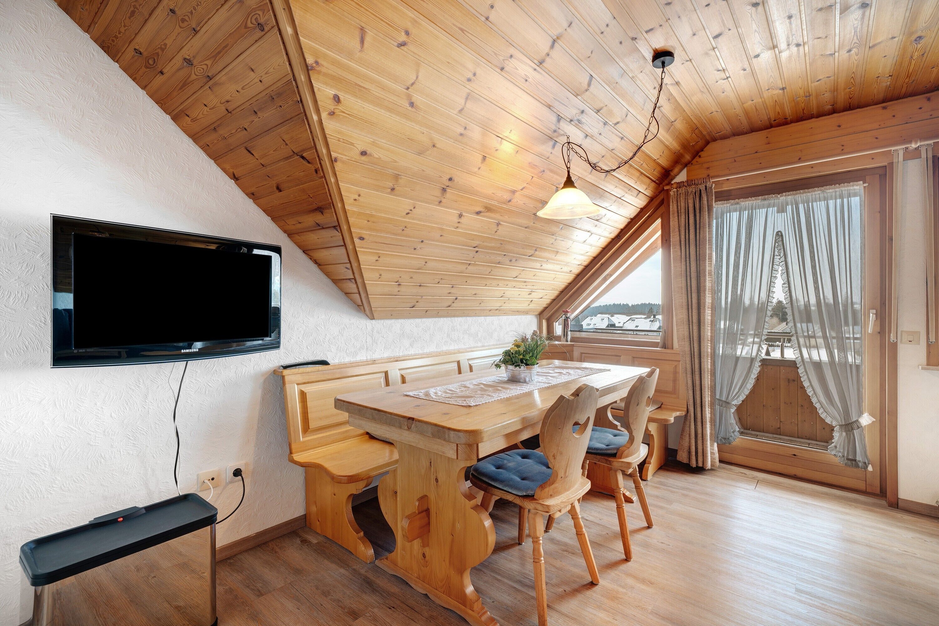 Ein Essbereich mit Holztisch, Stühlen und einem an der Wand befestigten Fernseher.