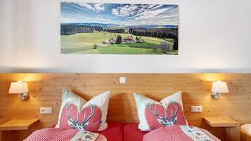 A room with a bed, two bedside tables, a wall-mounted lamp, and a framed landscape painting.