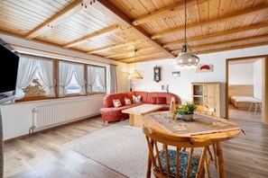 A spacious living area with a wooden ceiling, a red sofa, a wooden dining table, and a view through large windows. - Apartment 'Kandelblick Mit 60qm' with Mountain View, Private Terrace and Wi-Fi (Furtwangen im Schwarzwald)