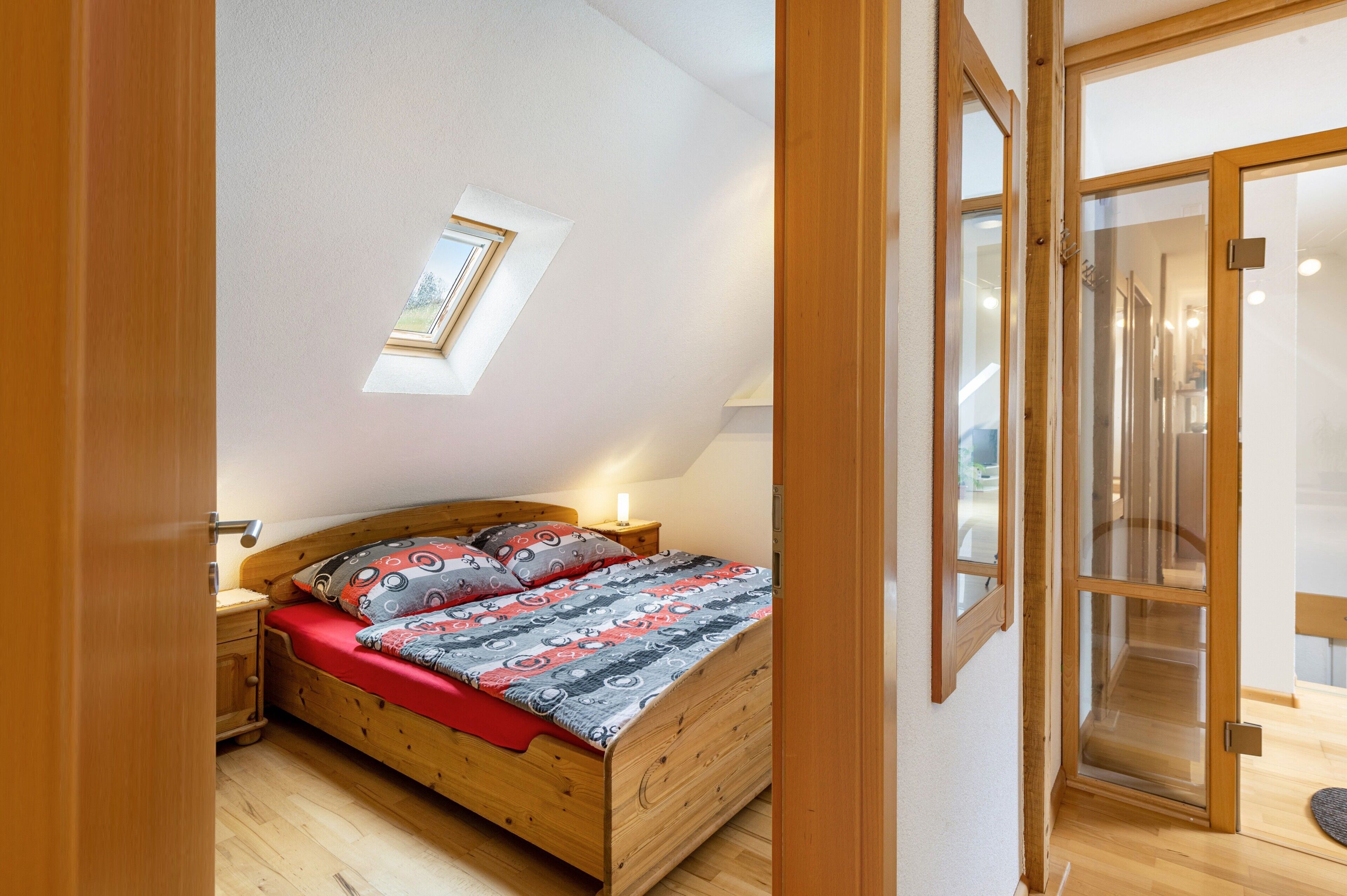 Une chambre à coucher avec un lit en bois, une lucarne et une porte-fenêtre coulissante donnant sur une salle de bain.