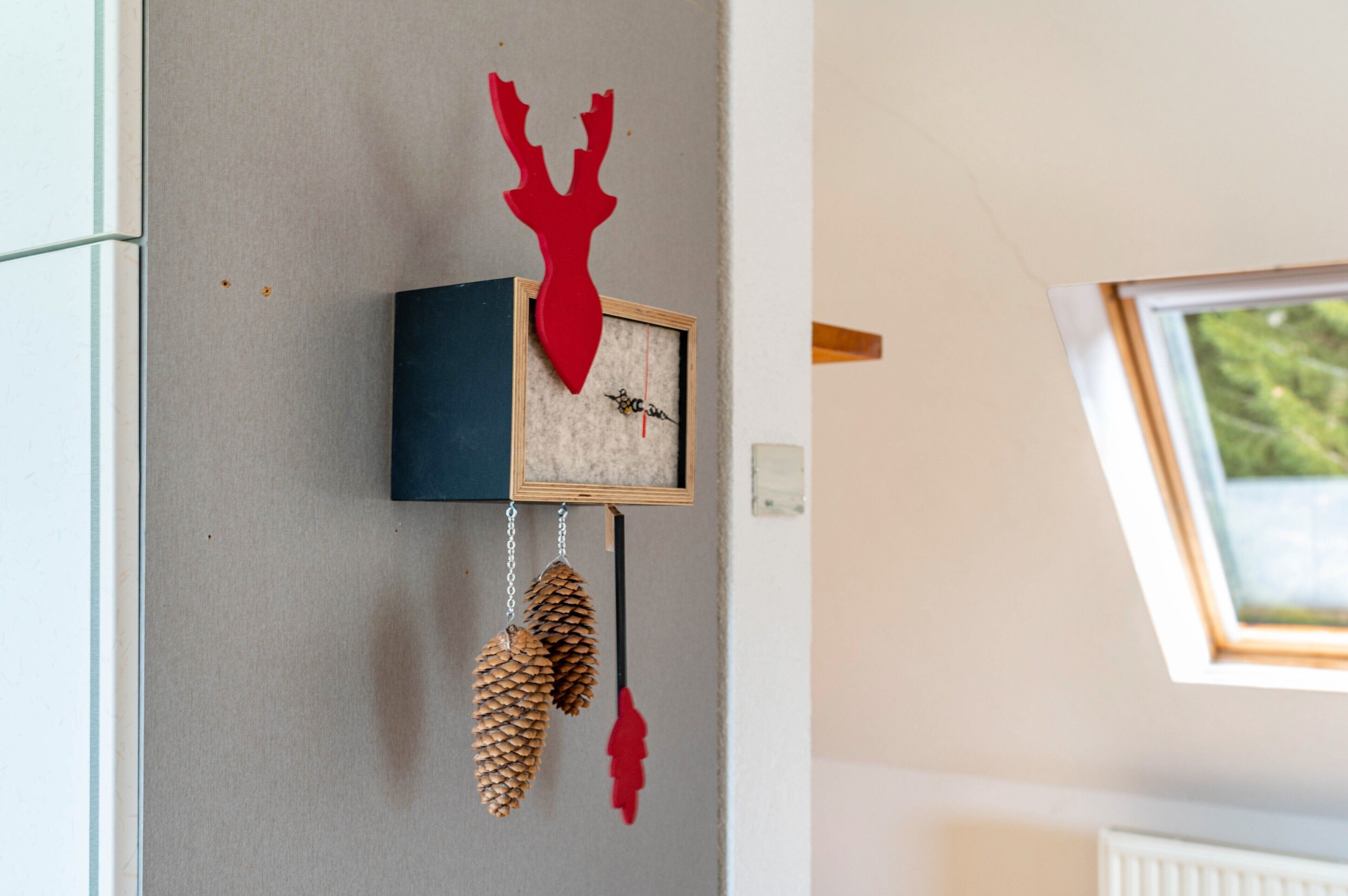 Un reloj de pared con un ciervo rojo, piñas y un cuadro enmarcado.