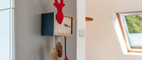 Un reloj de pared con un ciervo rojo, piñas y un cuadro enmarcado.
