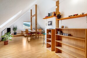 A spacious room with a dining area, wooden shelves, and a large window with a view. - Apartment 'Buche' with Mountain View, Shared Terrace and Wi-Fi (Todtnau)