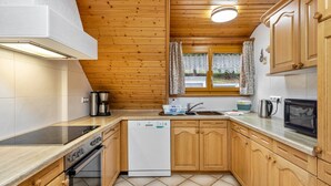Une cuisine avec des meubles de rangement en bois, un lave-vaisselle, une cuisinière, un four à micro-ondes et une fenêtre avec des rideaux.