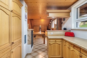 Une cuisine avec des meubles de rangement en bois, un sol carrelé, une table à manger et une fenêtre.