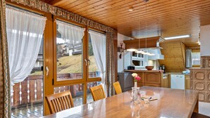 Une table à manger en bois avec des chaises, un coin cuisine et une vue sur une terrasse en bois.