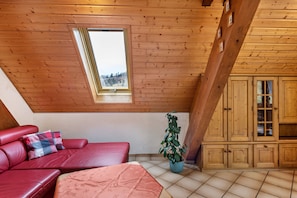 Une pièce avec un plafond en pente, un canapé en cuir rouge, une plante en pot et des meubles en bois.
