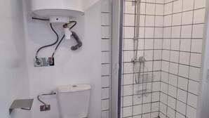 Kylpyhuone, jossa on wc, suihku ja valkoisilla laatoilla päällystetty seinä.