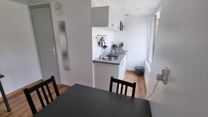 Kompakti keittiö, jossa on pesuallas, liesi ja kaapit. Etualalla on ruokapöytä ja tuolit.
