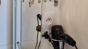 Pyöreäreunainen peili, hiustenkuivaaja ja pistorasia seinässä.