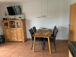 A dining area with a wooden table, black chairs, a television mounted on the wall, and a cabinet with drawers. - Apartment 'Elsternestchen' with Private Terrace, Shared Garden and Wi-Fi (Dornum)