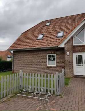 A brick house with a tiled roof, a white picket fence, and a bicycle rack. - Apartment 'Elsternestchen' with Private Terrace, Shared Garden and Wi-Fi (Dornum)
