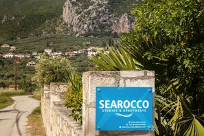 A sign for 'SEAROCCO STUDIOS & APARTMENTS' with a view of a road and houses in the background. - Searocco Studios & Apartments (Zakynthos)