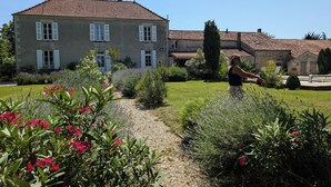 A stone building with a tiled roof, surrounded by a well-maintained garden with various plants and a gravel path. - Stylish Manor House, 6 Bed, Heated Outdoor Pool, Outdoor Kitchen, Sleeps 15 (Pouille)