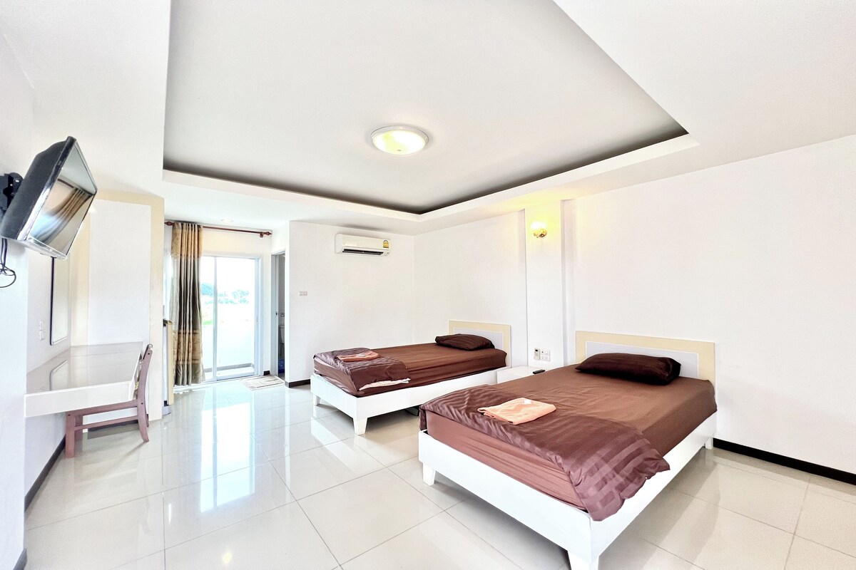 Una habitación de hotel con dos camas, un escritorio, una silla, un televisor y una ventana con cortinas.