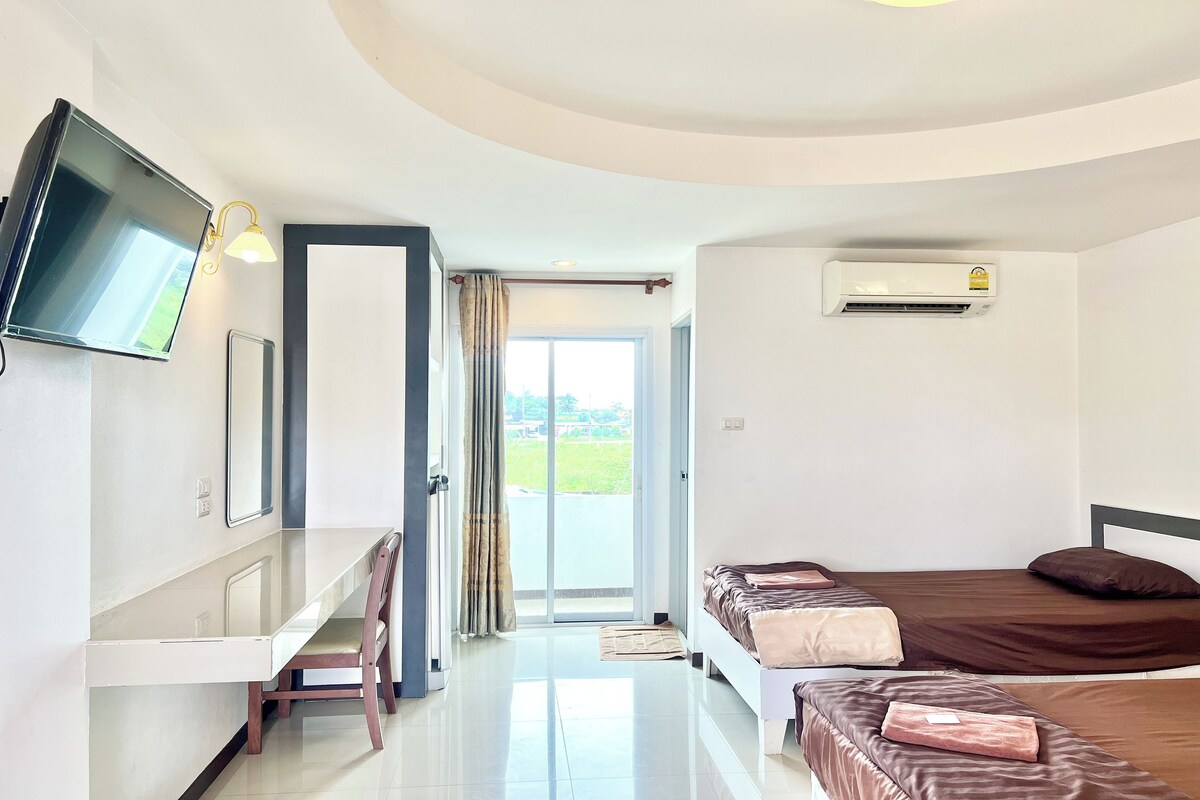 A hotel room with a flat-screen TV, a desk, two beds, and a sliding glass door leading to a balcony.