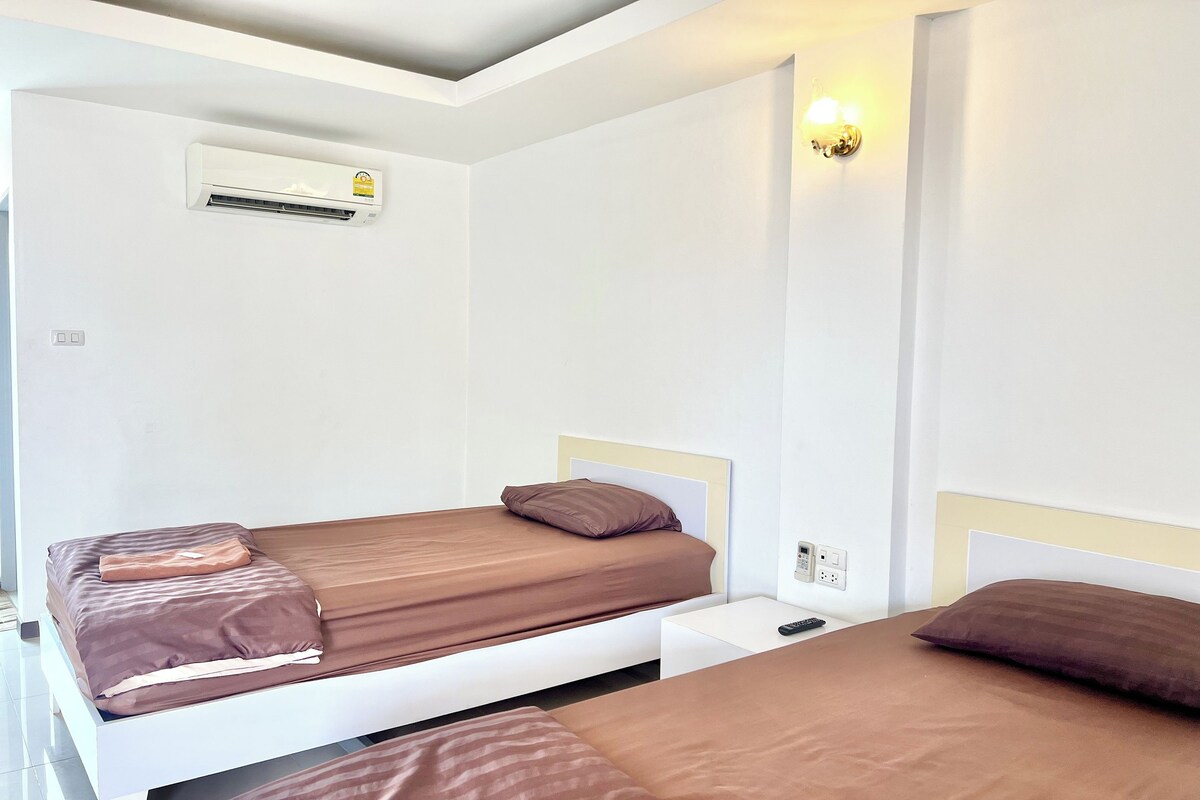 Habitación de hotel con dos camas, un equipo de aire acondicionado, una lámpara fijada a la pared y un enchufe.