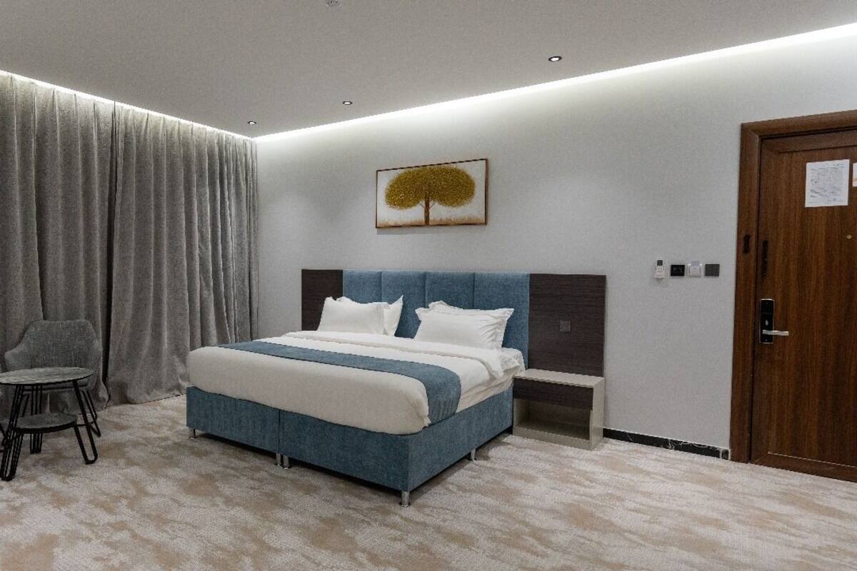 Een slaapkamer met een bed, een stoel, een klein tafeltje, een nachtkastje en een deur.