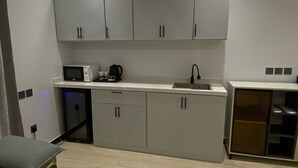 Et moderne køkken med lysegrå skabe, en mikrobølgeovn, en elkedel og en vask. En grå sofa er placeret i forgrunden.