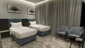 Et hotelværelse med to senge, et siddeområde med stole, et fladskærms-tv og billedkunst på væggene.