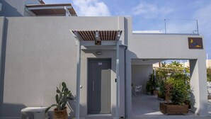 A modern building entrance with a grey door, a small covered porch, and a sign indicating a suite. - Alisahni Suite, Villa (Chania)