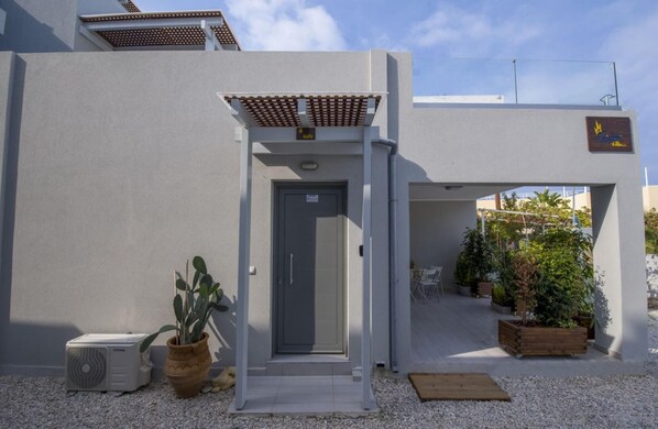 A modern building entrance with a grey door, a small covered porch, and a sign indicating a suite.