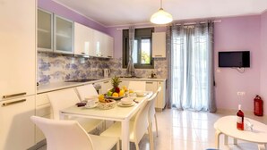 A modern kitchen with white cabinets, a tiled backsplash, and a dining area with a table set for breakfast. - Alisahni Suite, Villa (Chania)