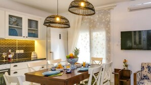 A modern kitchen with white cabinets, a built-in oven, and a dining area with a wooden table and white chairs. - Alisahni Villa, Villa (Chania)