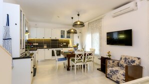 A modern kitchen with white cabinets, a dining area with a table and chairs, and a living area with a sofa and a TV mounted on the wall. - Alisahni Villa, Villa (Chania)