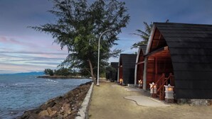 A coastal walkway with wooden cabins, a rocky shoreline, and a street lamp. - Nemuru Grand Anyer Palazo (Anyer)
