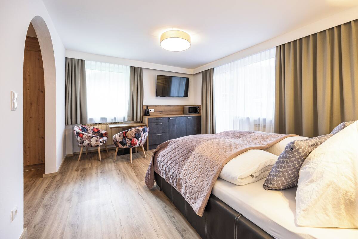 A hotel room with a bed, a desk, a chair, a television, and a kitchenette.