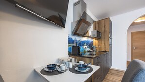 Una kitchenette compacta con estufa, microondas y armarios de madera. Se ha dispuesto una mesa de comedor con platos, tazones y vasos.
