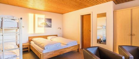 A bedroom with a wooden ceiling, a bed with white linens, a wooden wardrobe, and a seating area with two chairs.