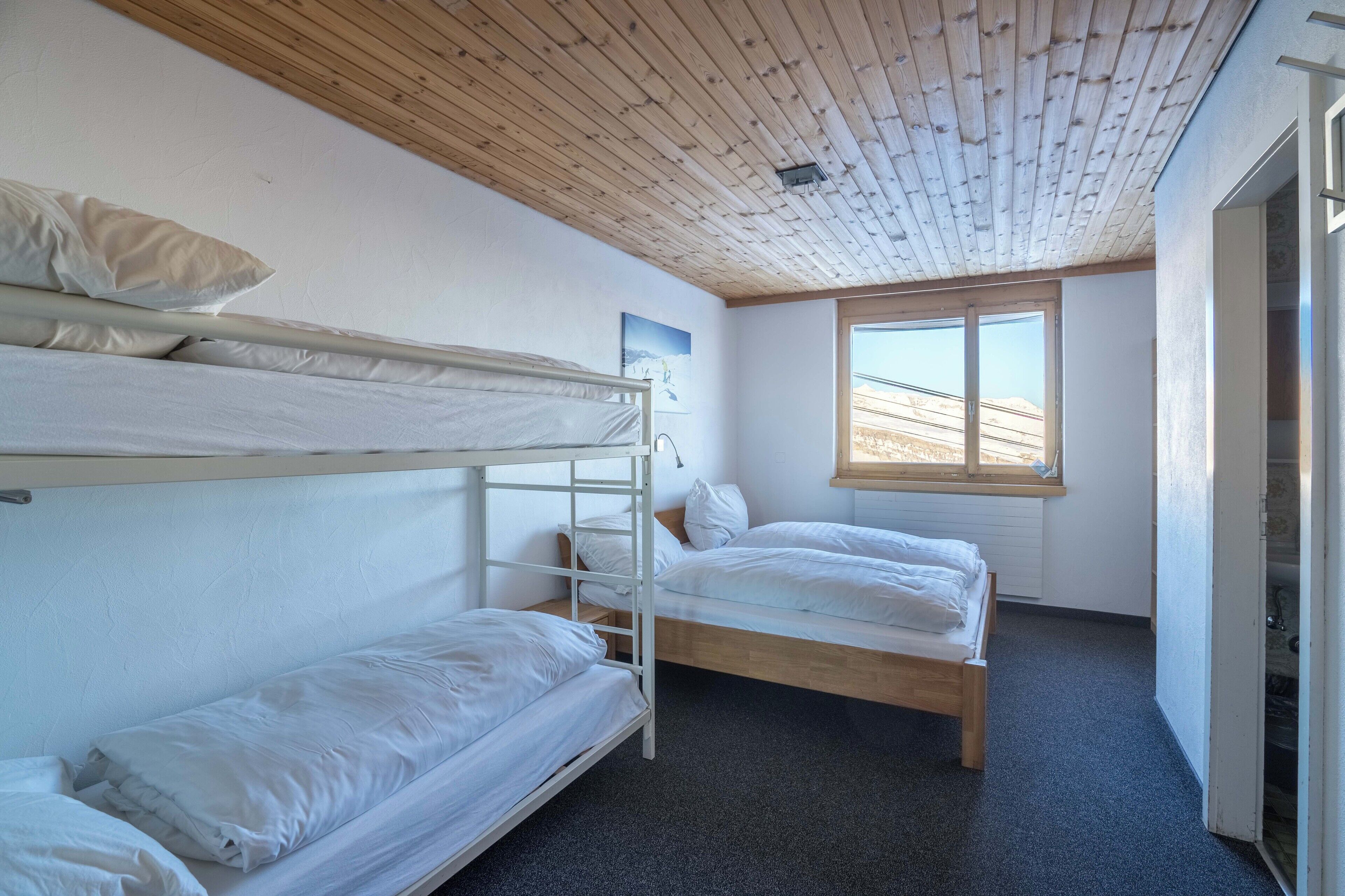 Una camera con letto a castello, soffitto in legno, una finestra con vista e una porta sulla destra.