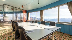 A conference room with a large table, chairs, and a view of mountains through the windows. - GALAAXY Mountain Hostel (Falera)