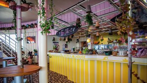 A counter with a sign reading "Beach House" in a cafe setting with hanging plants and a patterned floor. - GALAAXY Mountain Hostel (Falera)