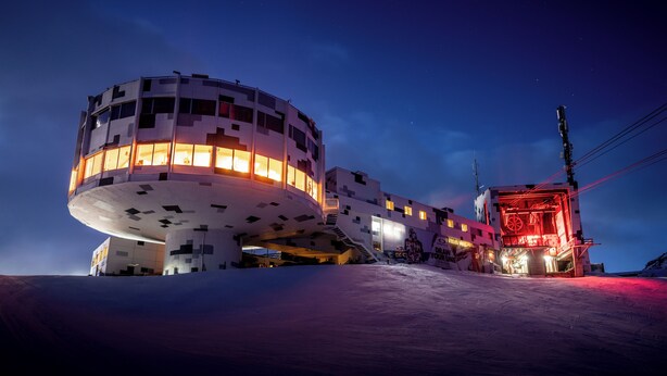 A modern building with a unique circular structure and a red-lit section. - GALAAXY Mountain Hostel (Falera)