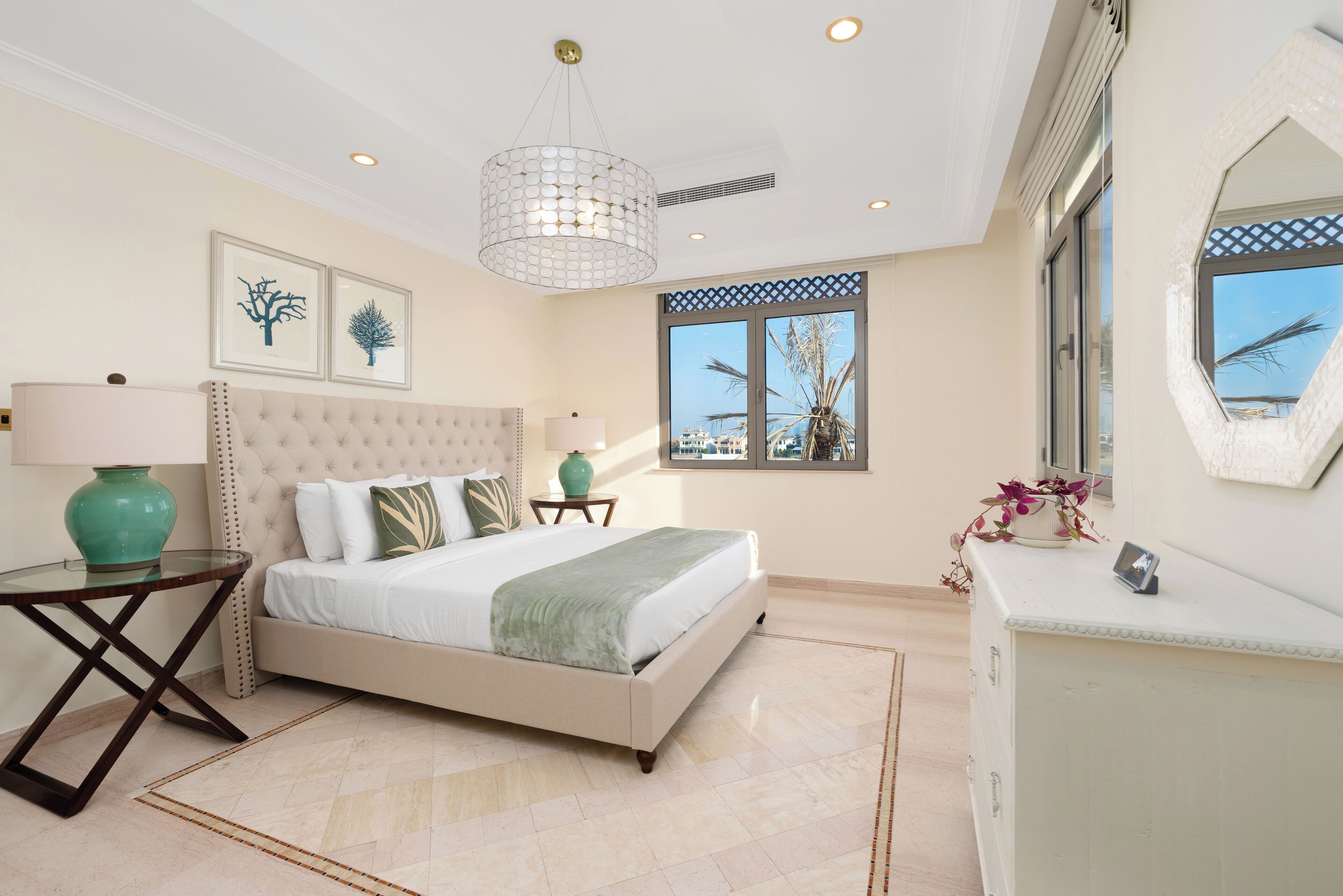 A bedroom with a large bed, a bedside table with a lamp, a window with a view, and a decorative mirror.