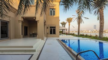 A modern building with a swimming pool, palm trees, and a view of the city skyline.